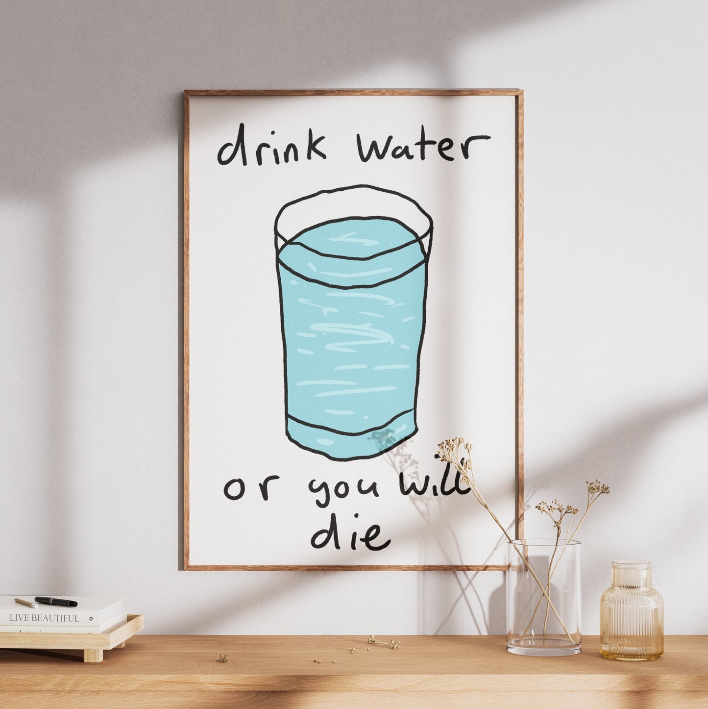 Framed poster with a glass of water and text 'drink water or you will die' on a wooden surface.